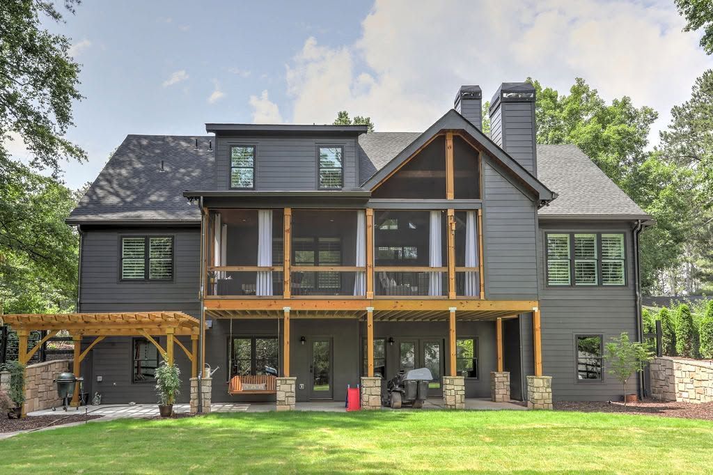 Large modern house with dark siding, wood accents, and a spacious green lawn.