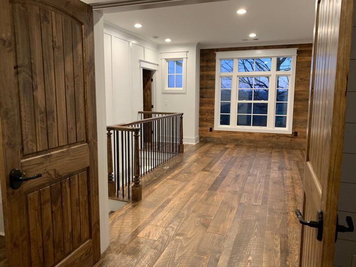Wood-floored hallway with white walls, rustic doors, railing, and a large window at the end