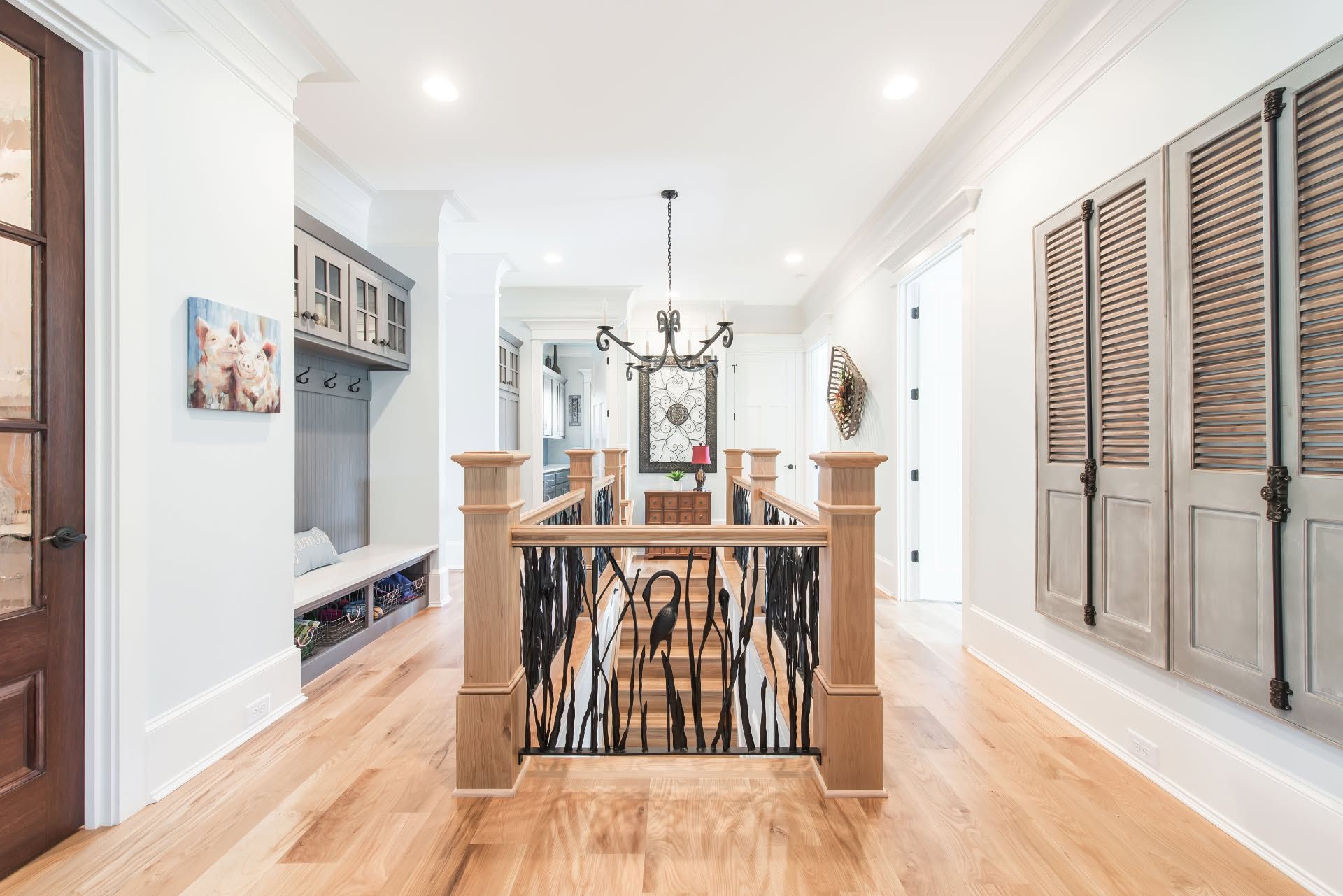 Bright hallway with wood floors, staircase railing, and louvered closet doors leading to a dining area.