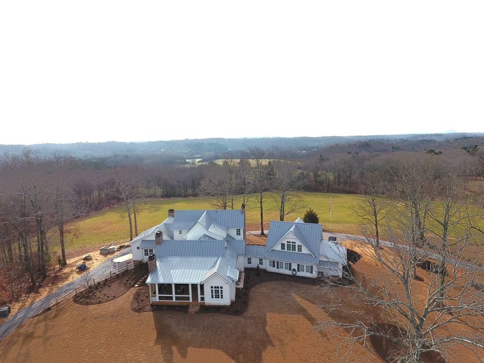 Aerial view of a large white house with a gray roof surrounded by bare trees and open fields.