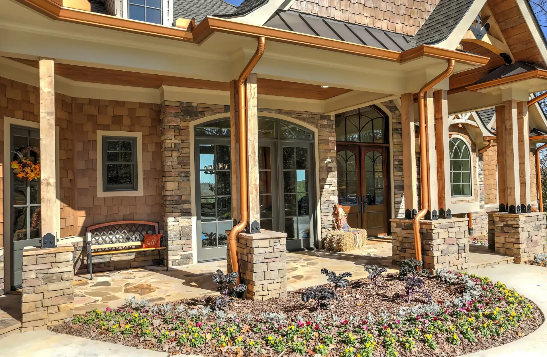 Brick house porch with stone columns, glass doors, and a flower bed in front