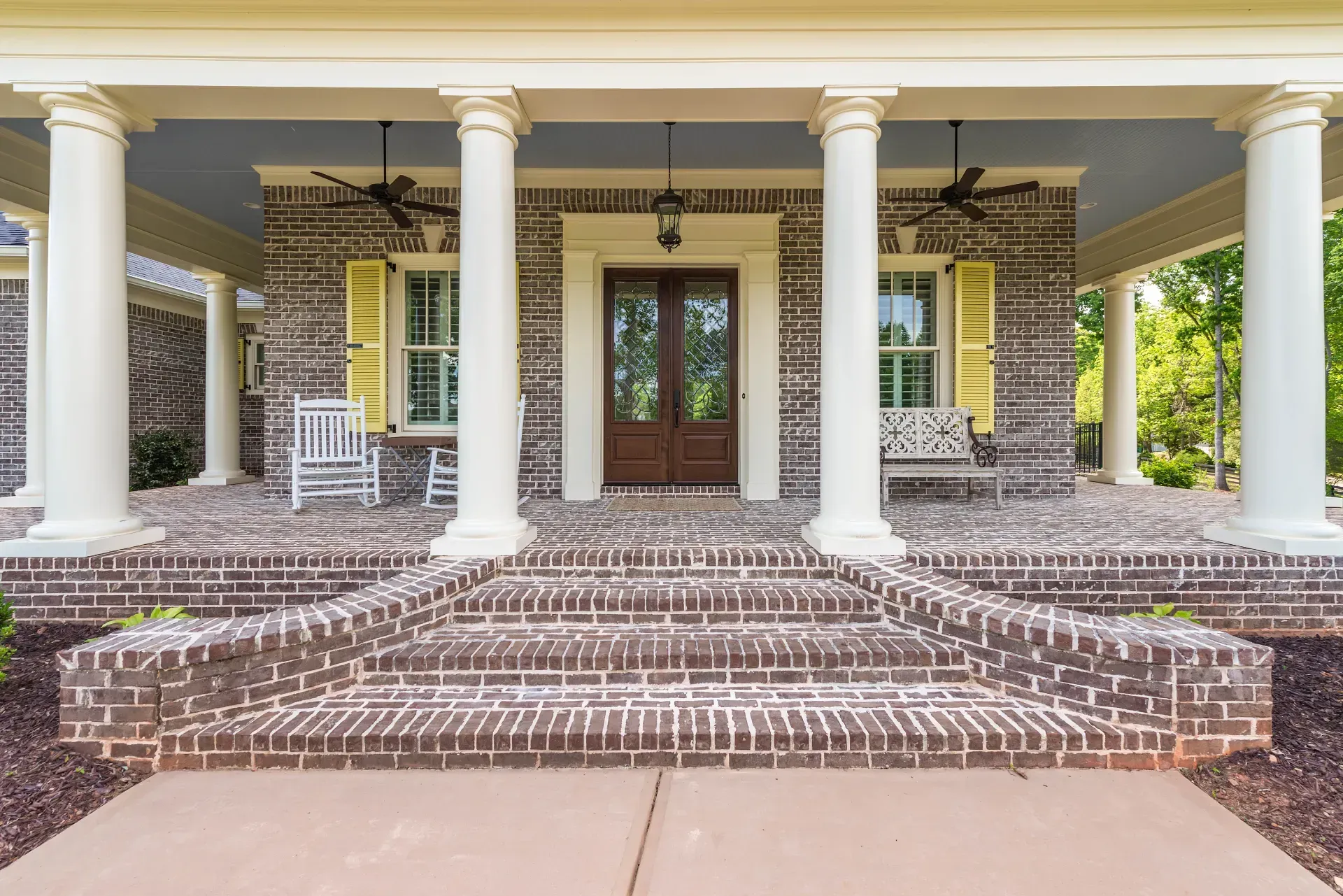 Brick front porch with white columns, steps, and double wooden doors on a yellow house
