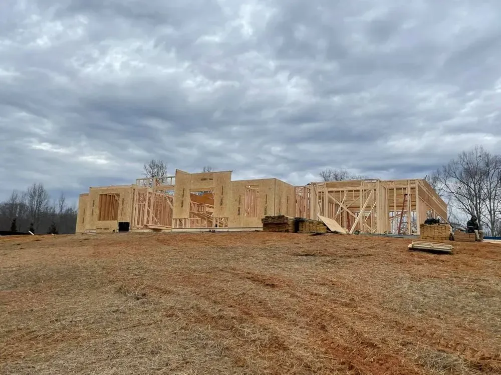 Wood-framed house under construction on a bare lot beneath a cloudy sky