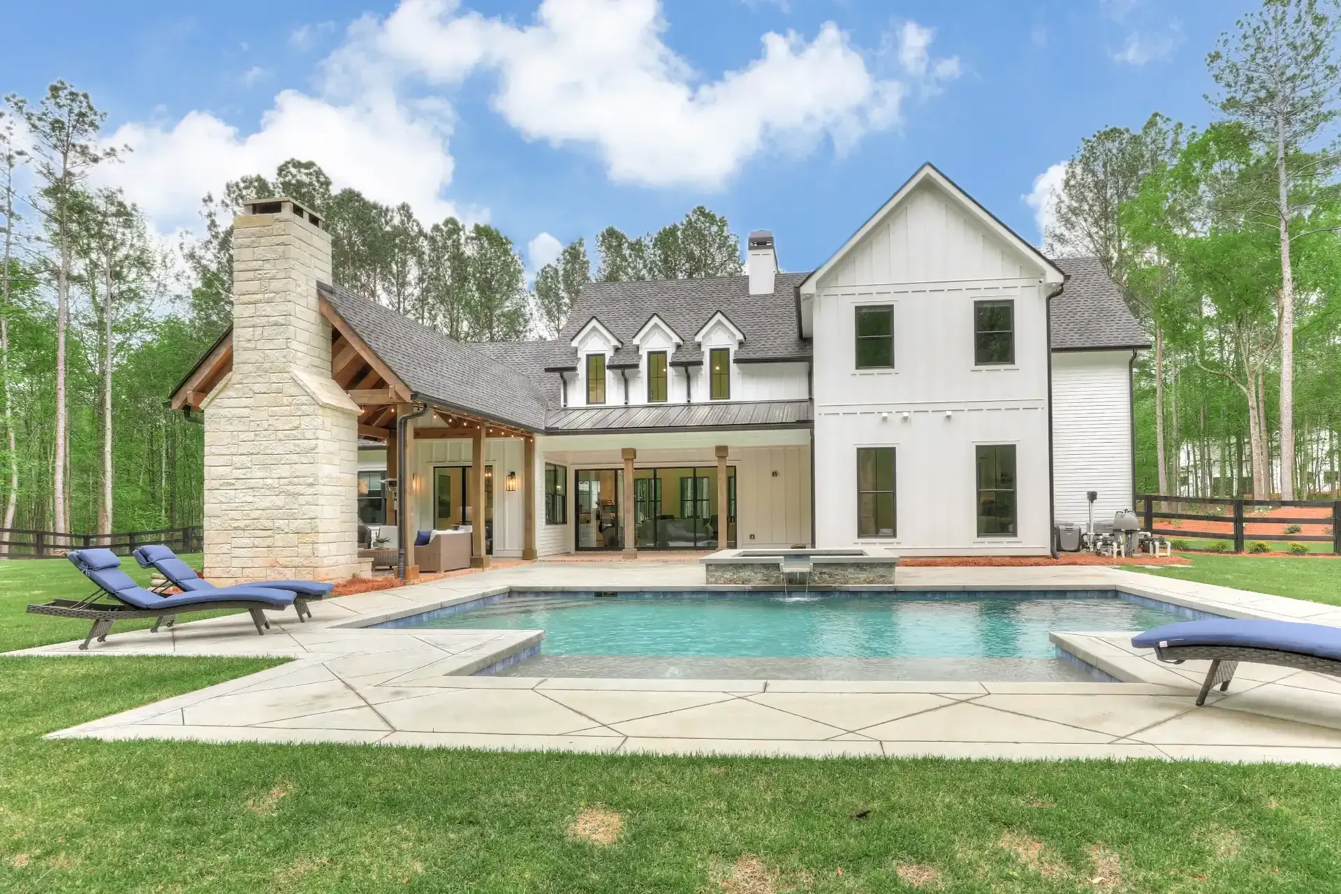 Luxury modern house with a backyard pool, patio, and lounge chairs under a bright sky