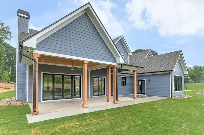 Blue-gray modern house with covered porch, black-framed windows, and green lawn