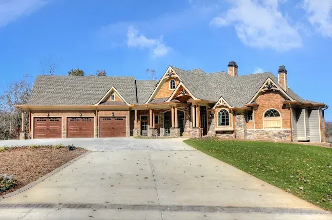 Large brick suburban house with a three-car garage and wide concrete driveway under a blue sky