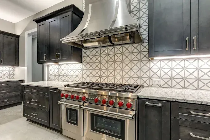 Modern kitchen with dark cabinets, stainless steel range hood, patterned backsplash, and double oven