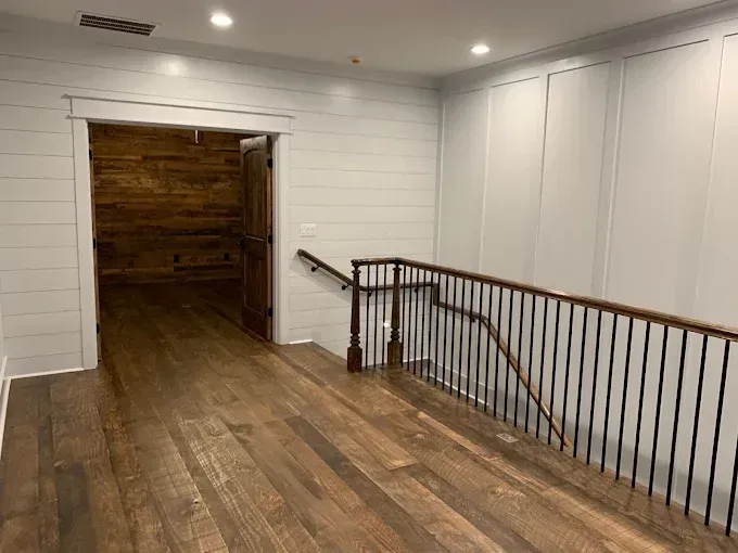 Wooden hallway with white walls, railings, and an open doorway leading to a darker room