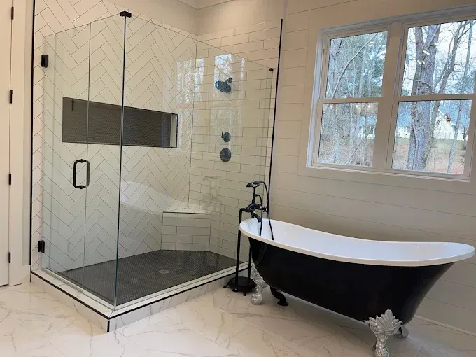 Modern bathroom with glass shower enclosure, black freestanding tub, and window with natural light