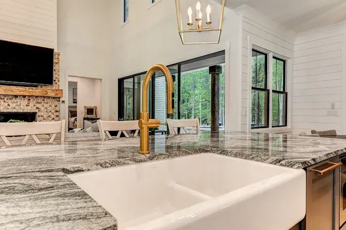 Bright modern kitchen with marble island, white chairs, black windows, and a farmhouse sink