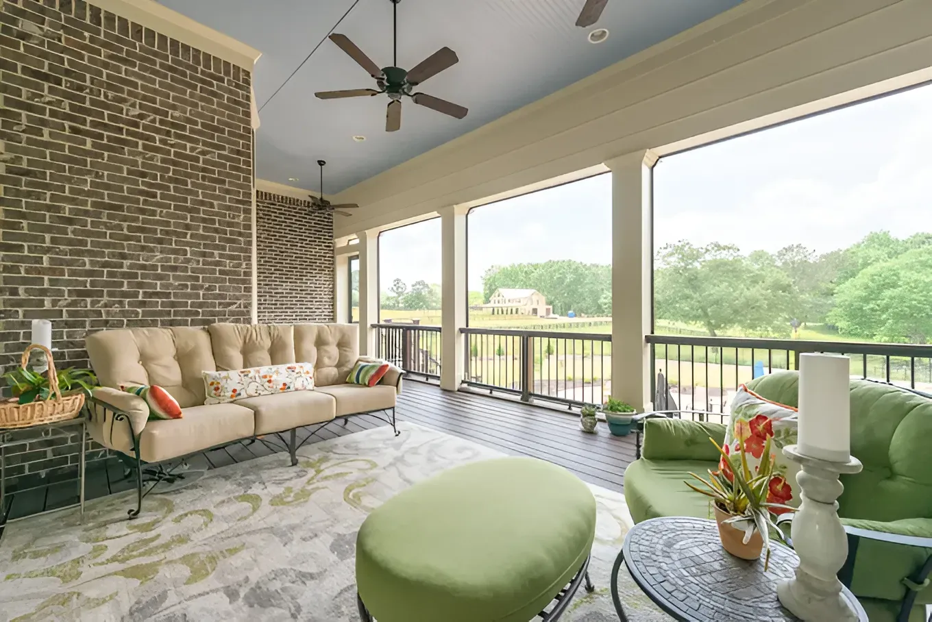 Bright screened porch with beige sofa, green ottoman, brick wall, and wooded view beyond railing