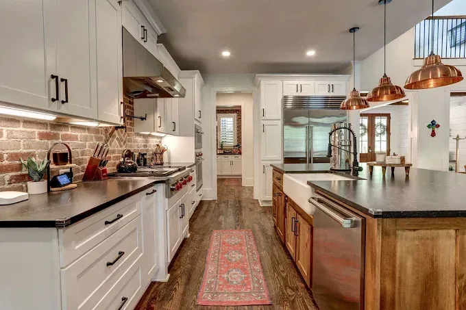 Bright modern kitchen with white cabinets, brick backsplash, wood island, and copper pendant lights