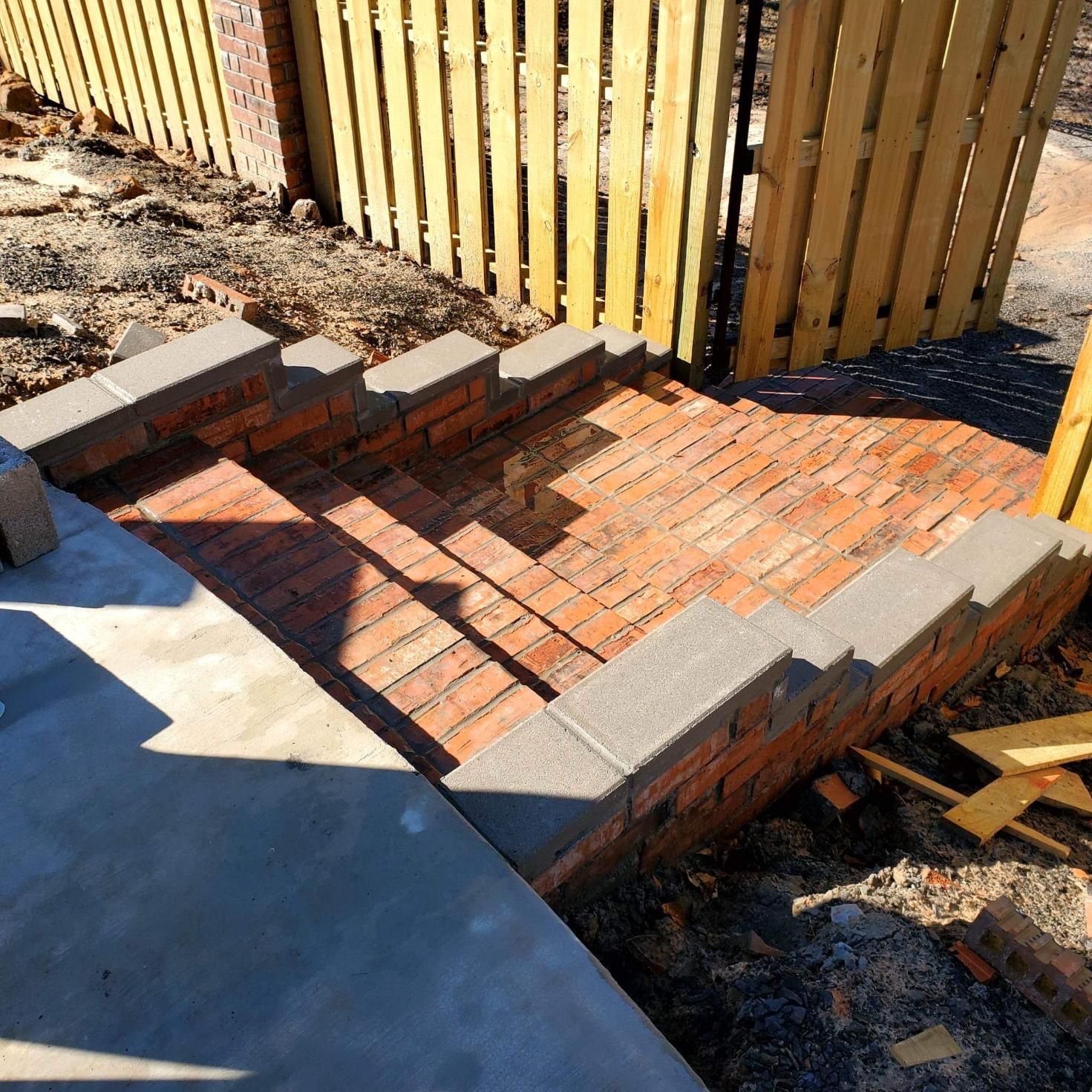 A wooden fence is behind a set of brick stairs.
