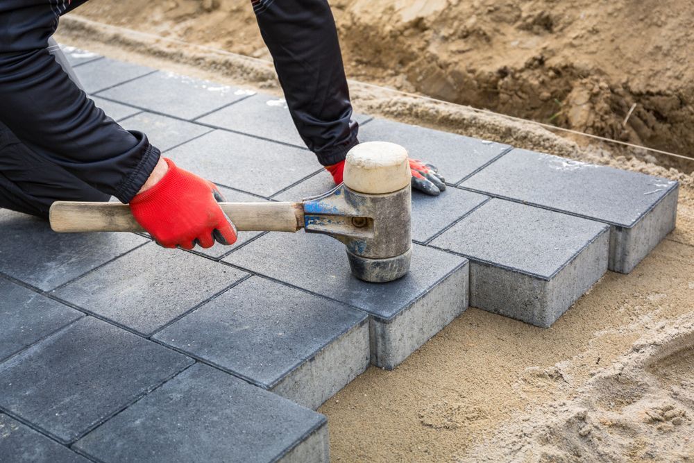 A worker is installing concrete paver blocks with rubber hammer.