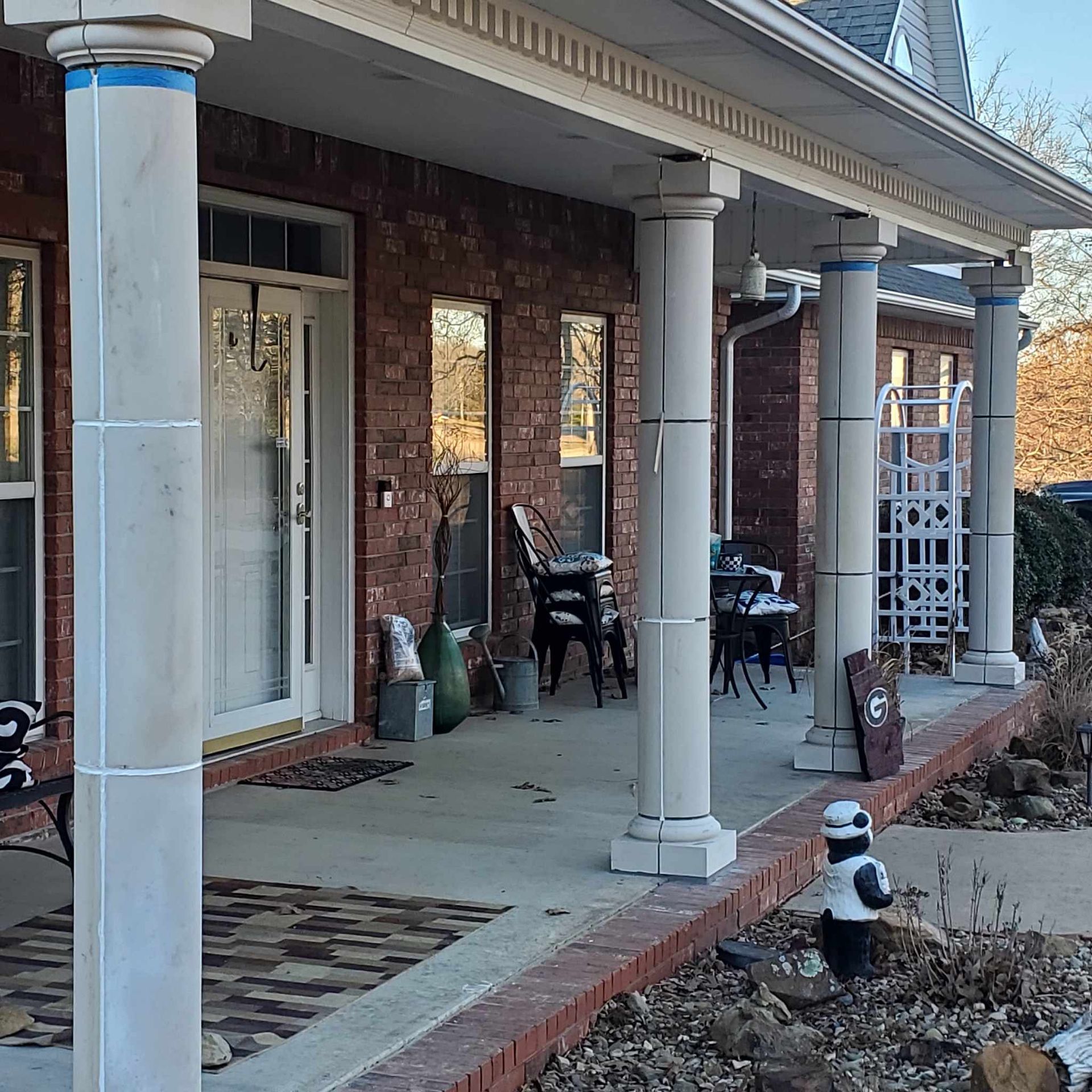 A brick house with a porch with columns and chairs.