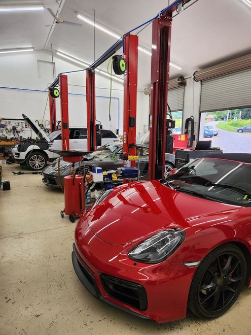 A red Porsche parked in a bright garage with other luxury cars undergoing maintenance under vehicle lifts. | Mountain European Auto Repair