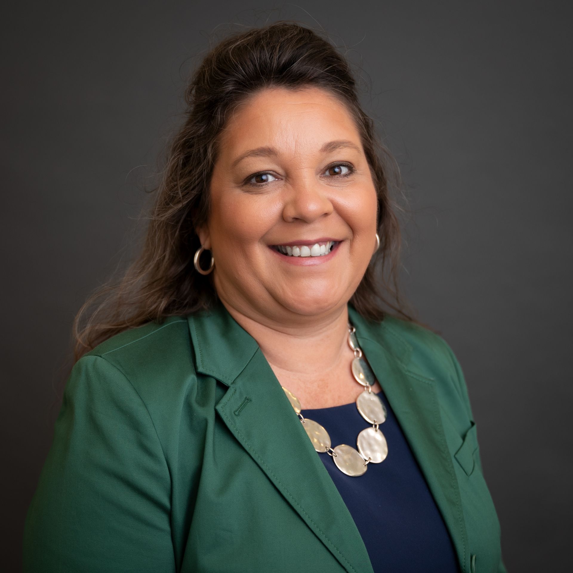 Smiling woman in a green blazer and navy top against a gray studio background