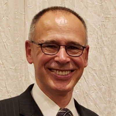 Smiling man in glasses and dark suit against a light curtain background