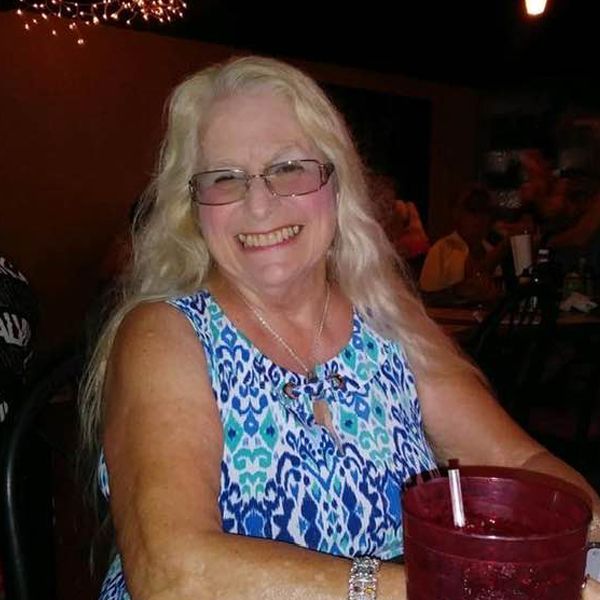 Smiling woman in a blue patterned top seated indoors with a red drink cup