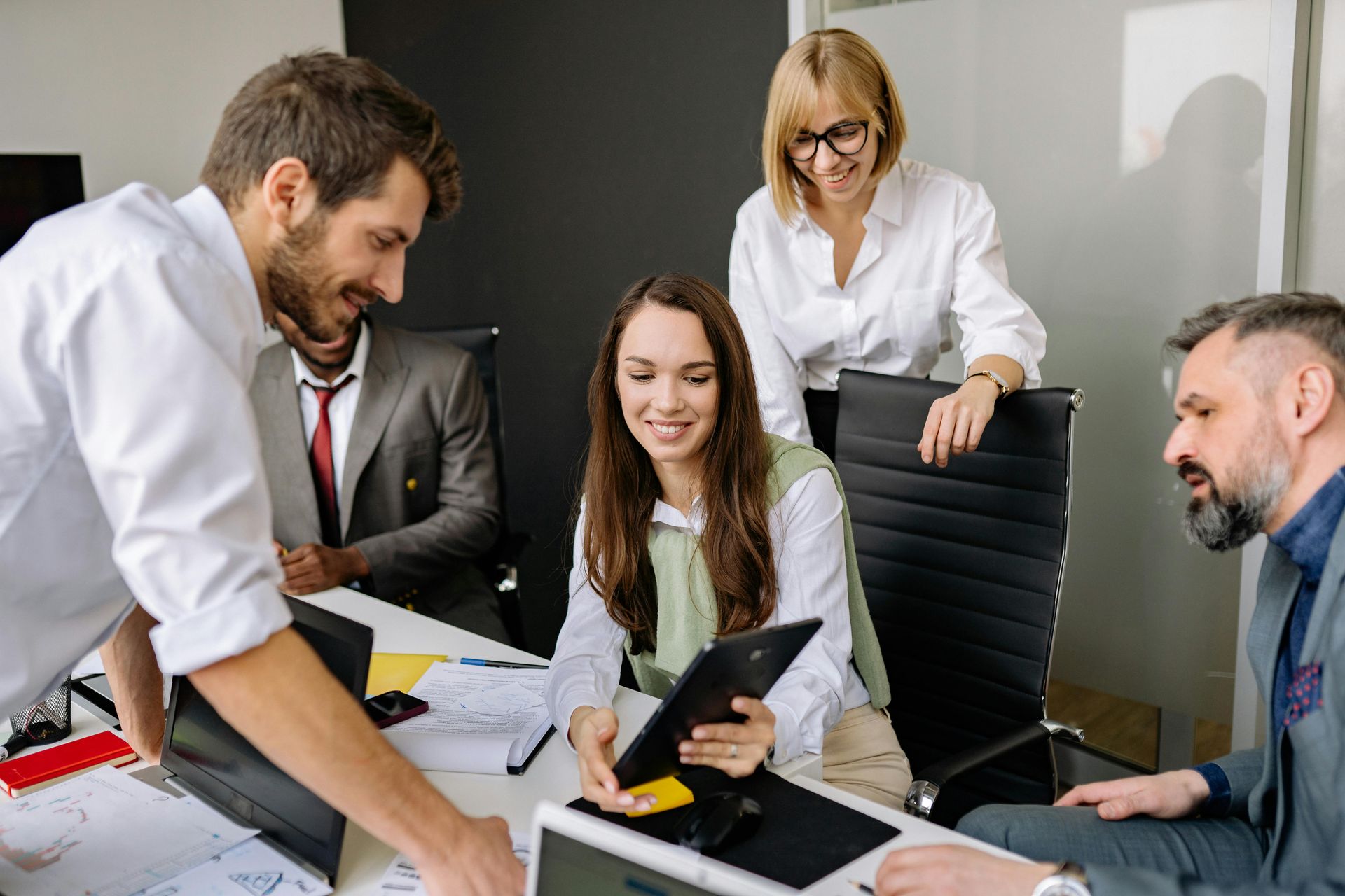 Colleagues gathered around a table in a meeting room, reviewing documents and a tablet.