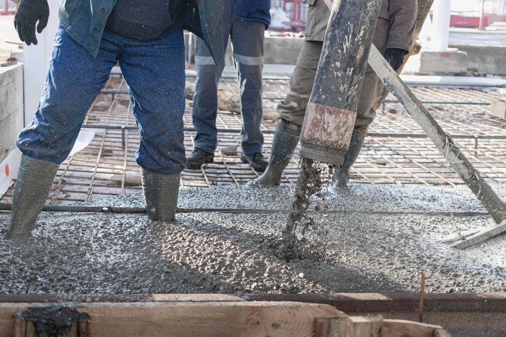 Workers pouring wet concrete onto a rebar grid at a construction site