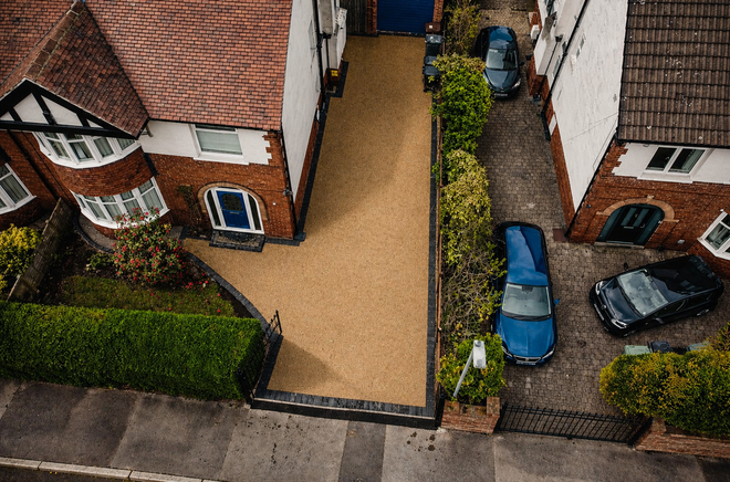 Aerial view of two houses with a tan driveway and parked cars beside a street