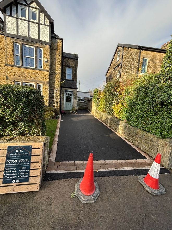 Driveway between stone buildings, blocked by red traffic cones and a low barrier under construction.