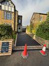 Driveway entrance between stone buildings, blocked by two orange cones and a low barrier.