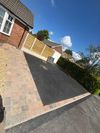 Driveway and front garden of a suburban house on a sunny day, with a white car and blue sky.