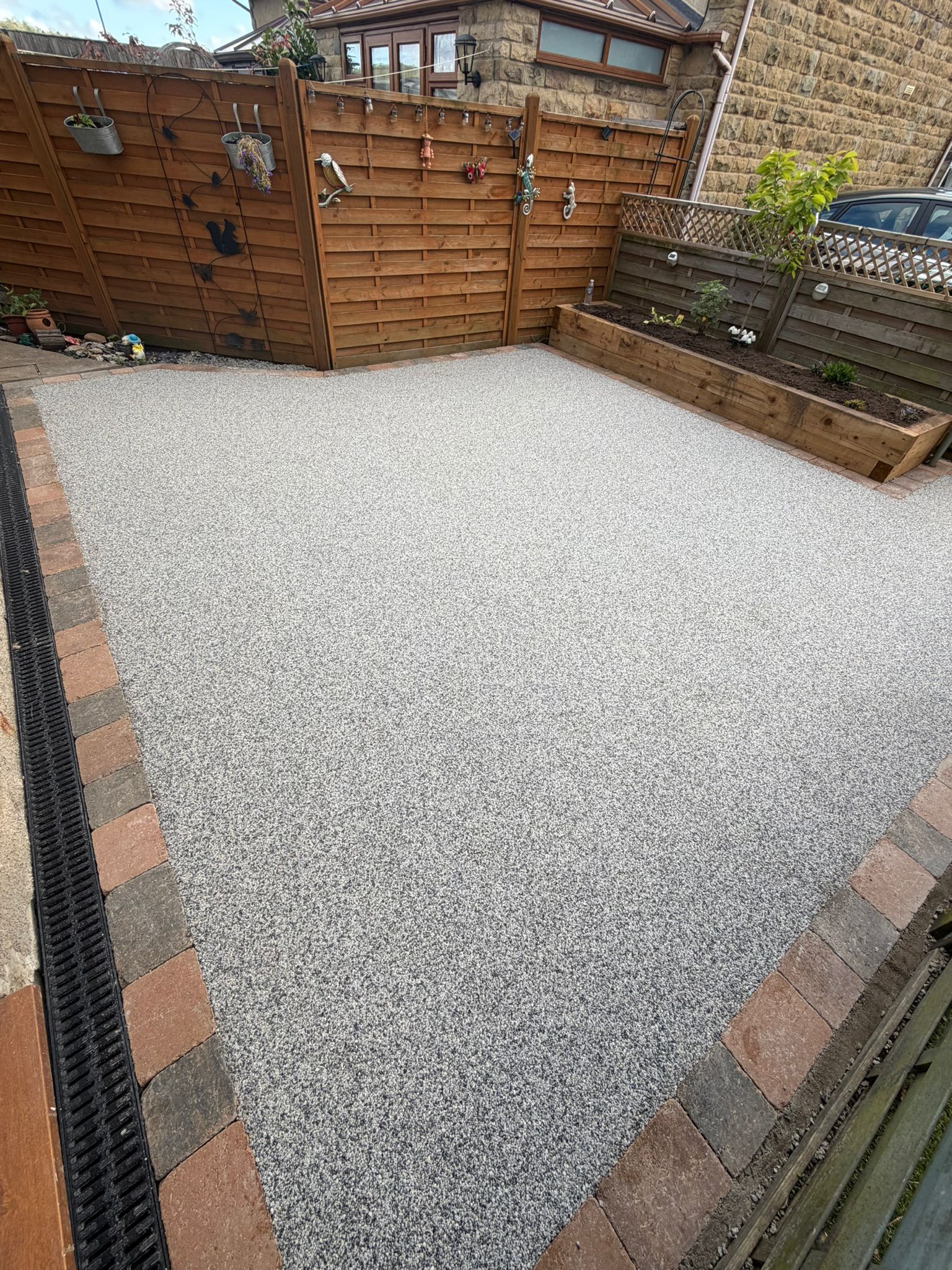 Small gravel-covered backyard patio bordered by brick, wooden fence, and raised planter bed.