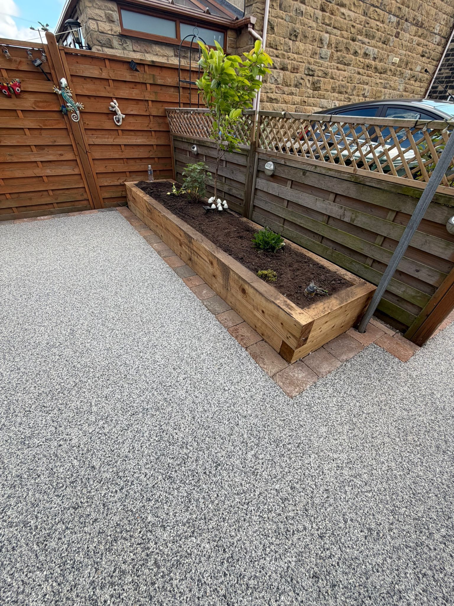 Raised wooden planter with a small tree in a gravel backyard next to a wood fence