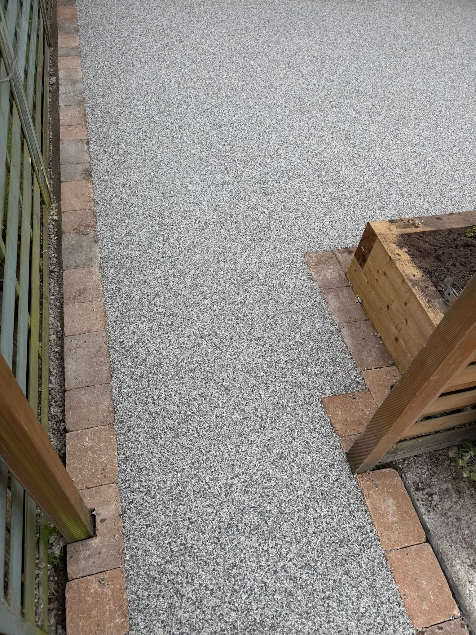 Gravel walkway bordered by brick and wooden planters on both sides.