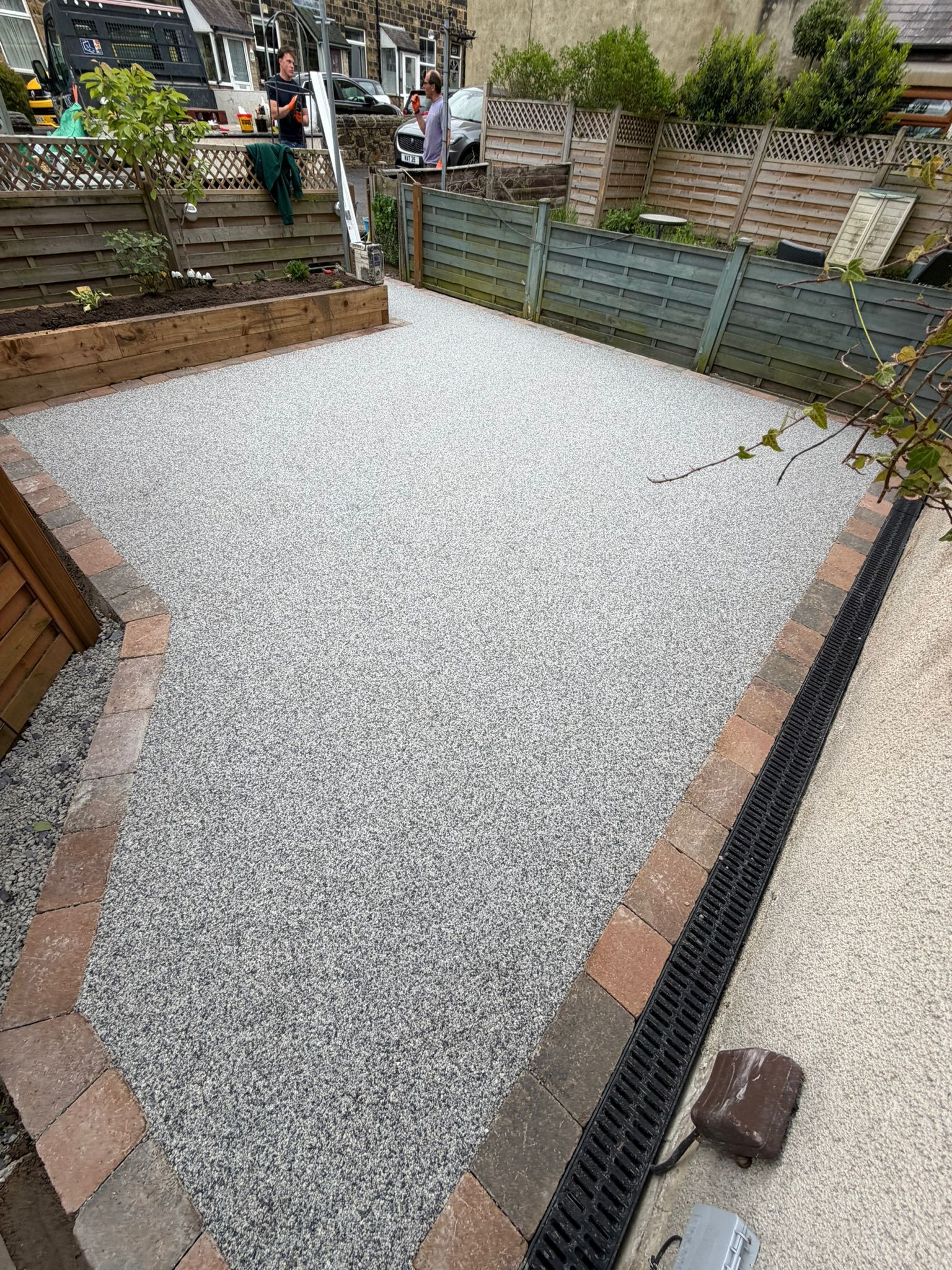 Gravel-covered backyard patio with retaining walls, steps, and neighboring fences.