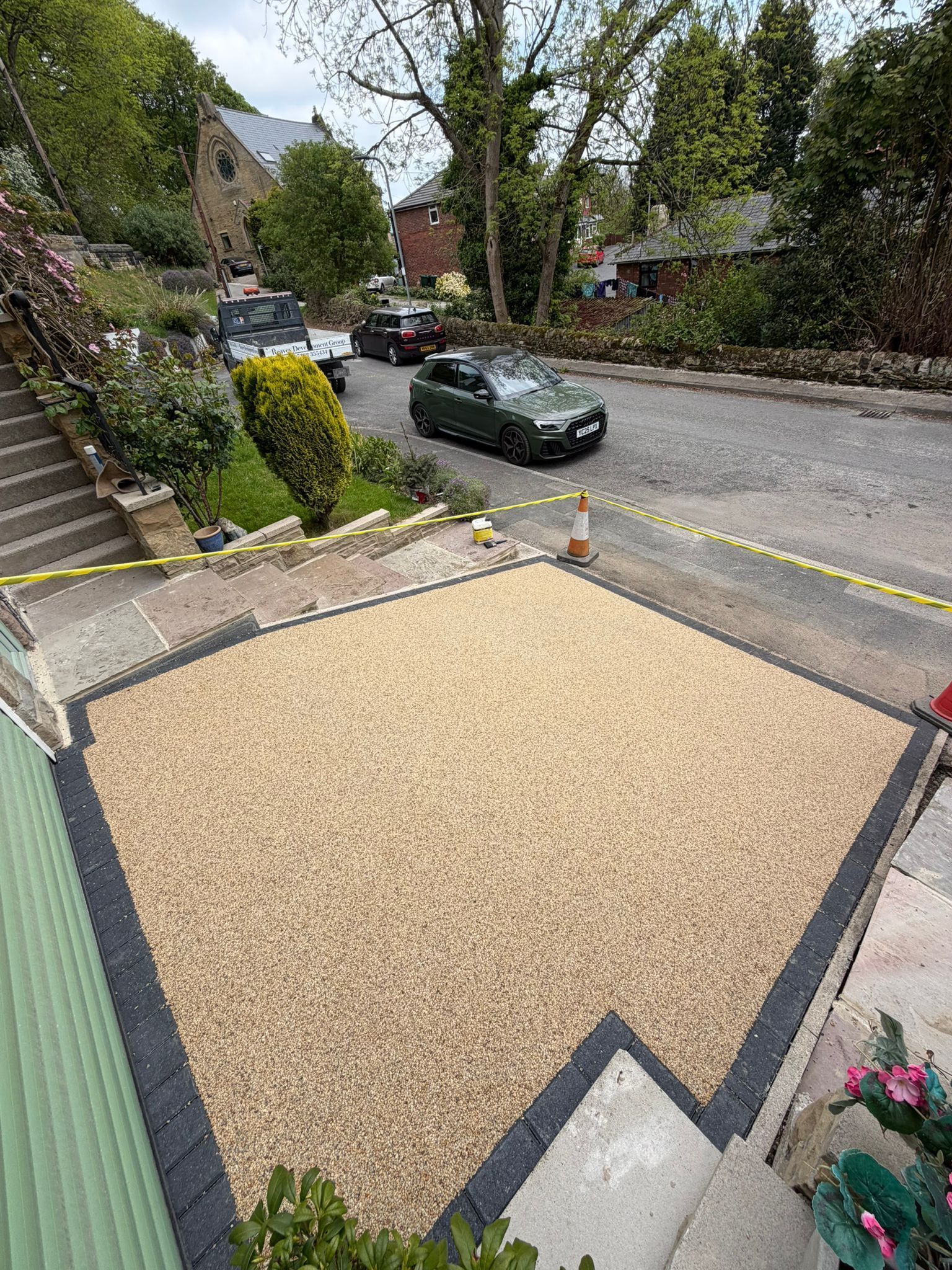 Gravel driveway with dark edging beside a quiet residential street and parked car.