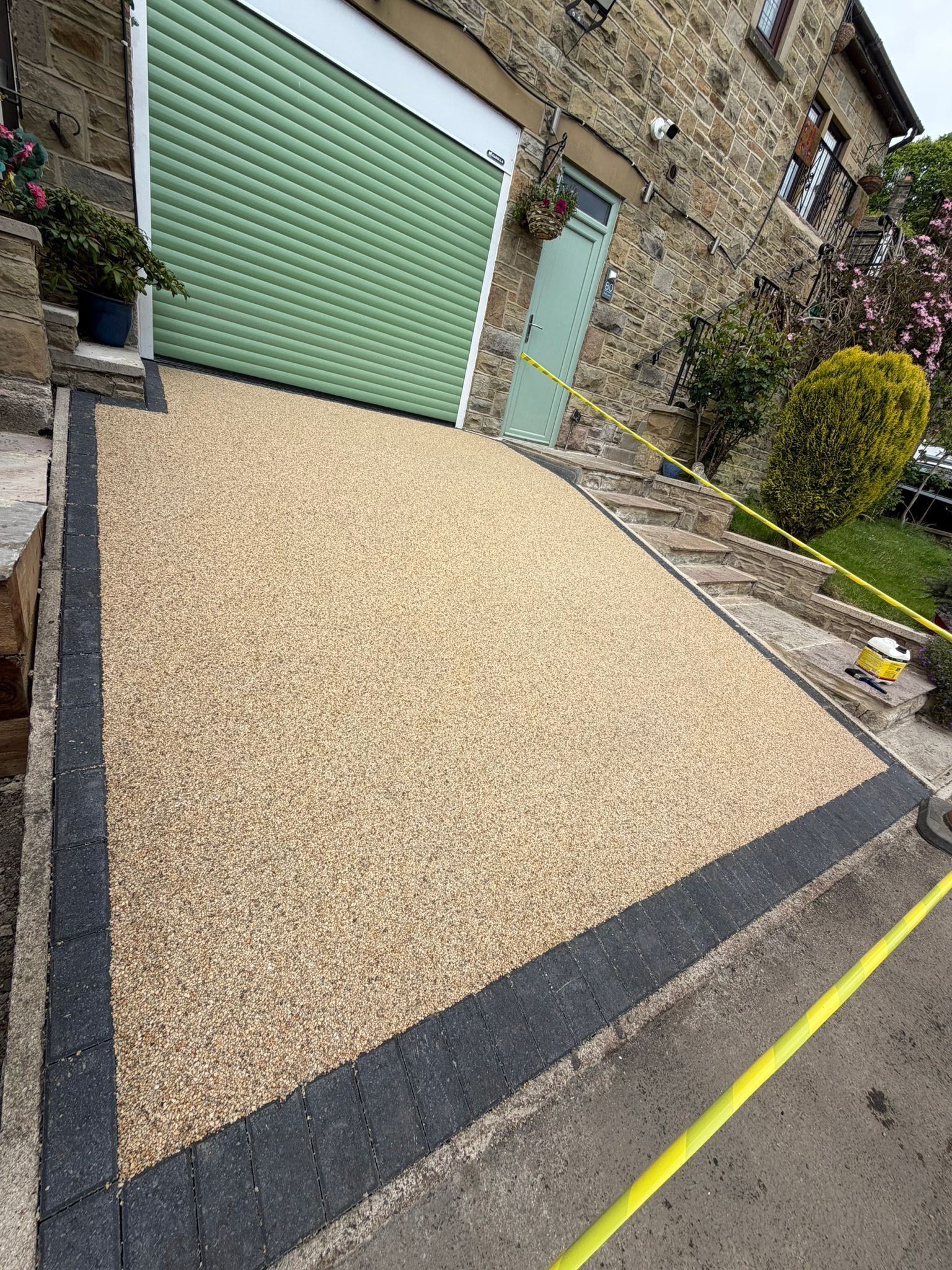 Resin driveway in front of a stone house with a green garage door and black edging.