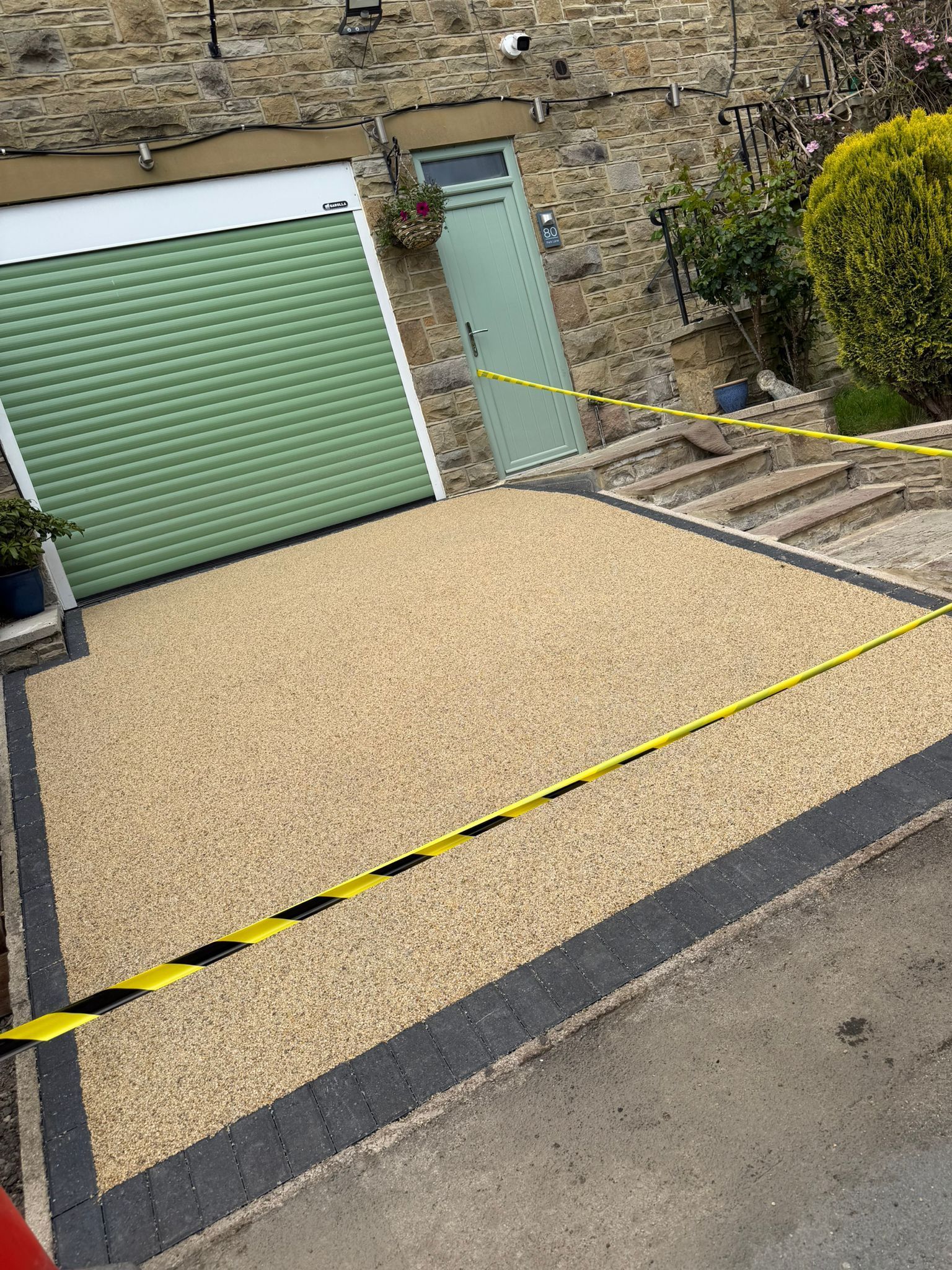 Cordoned-off driveway with green garage door, gravel area, and yellow-black caution tape across the entrance