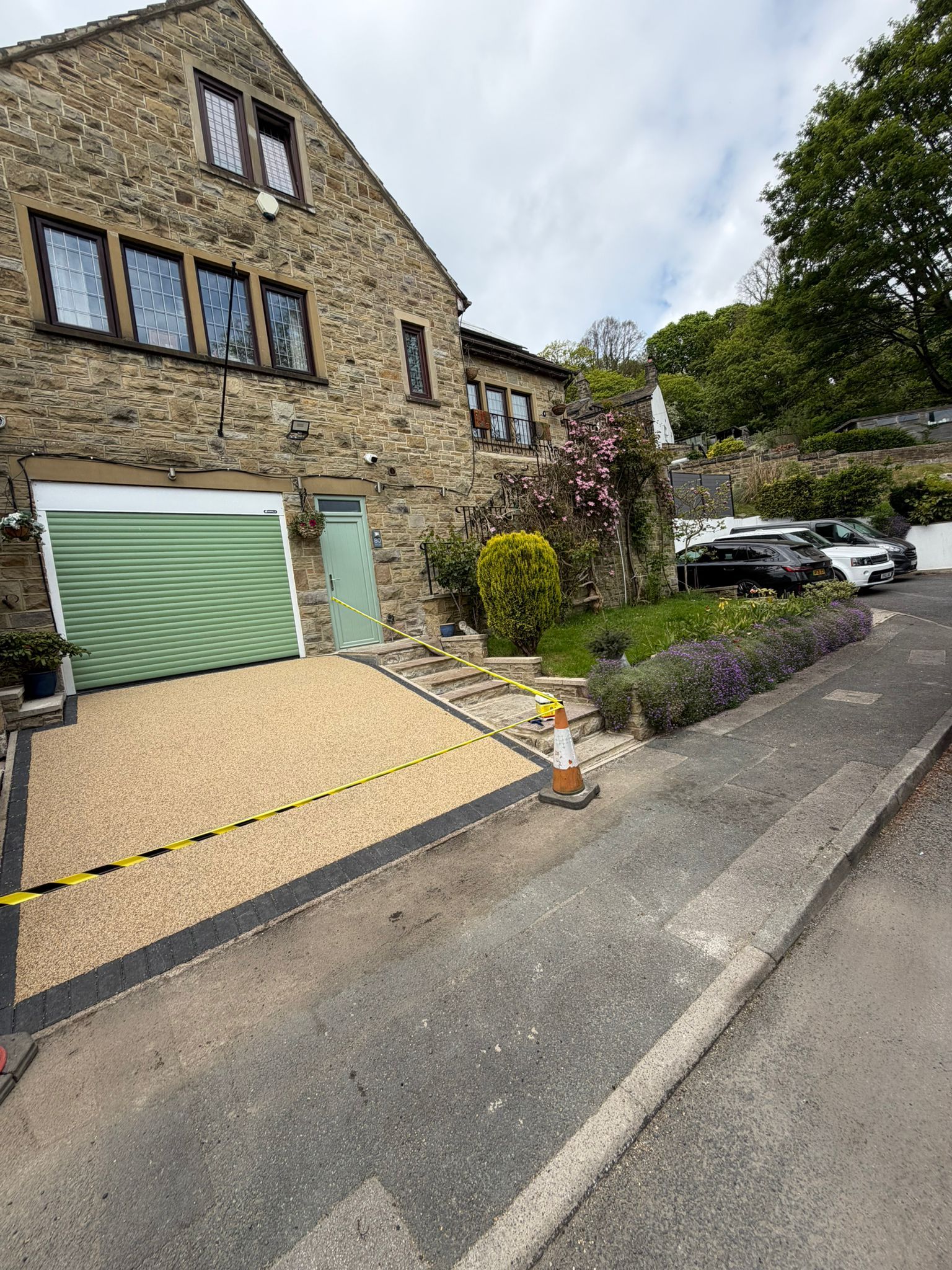Stone apartment building with green garage door, sloped driveway, and parked cars on a quiet street.