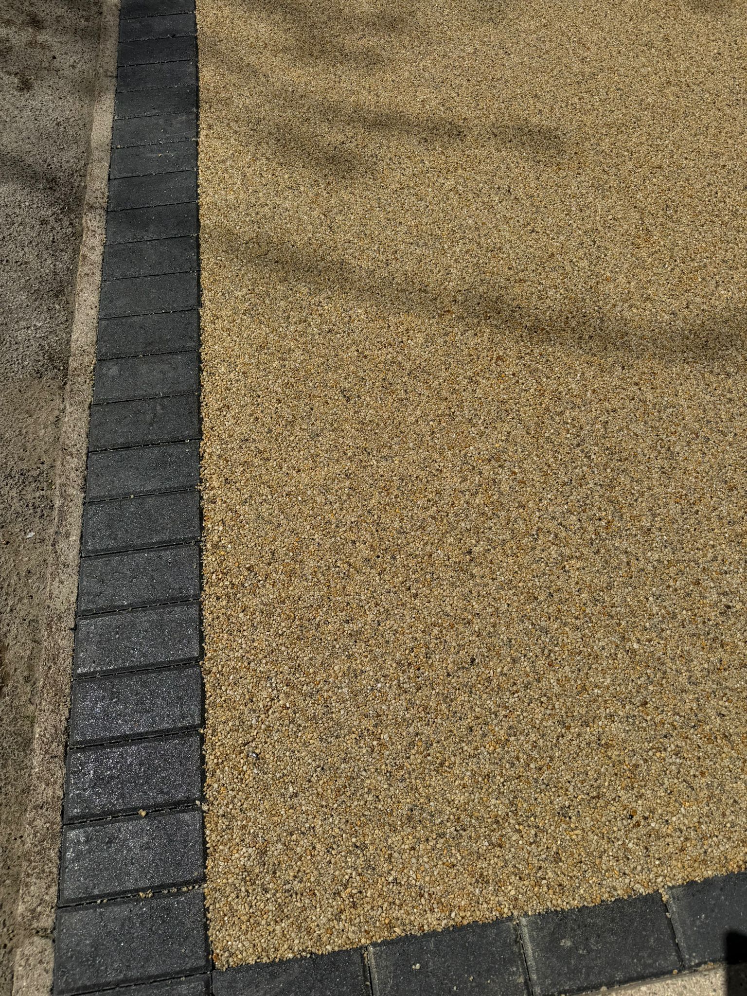 Curved gray brick border beside tan gravel paving on a sidewalk or driveway