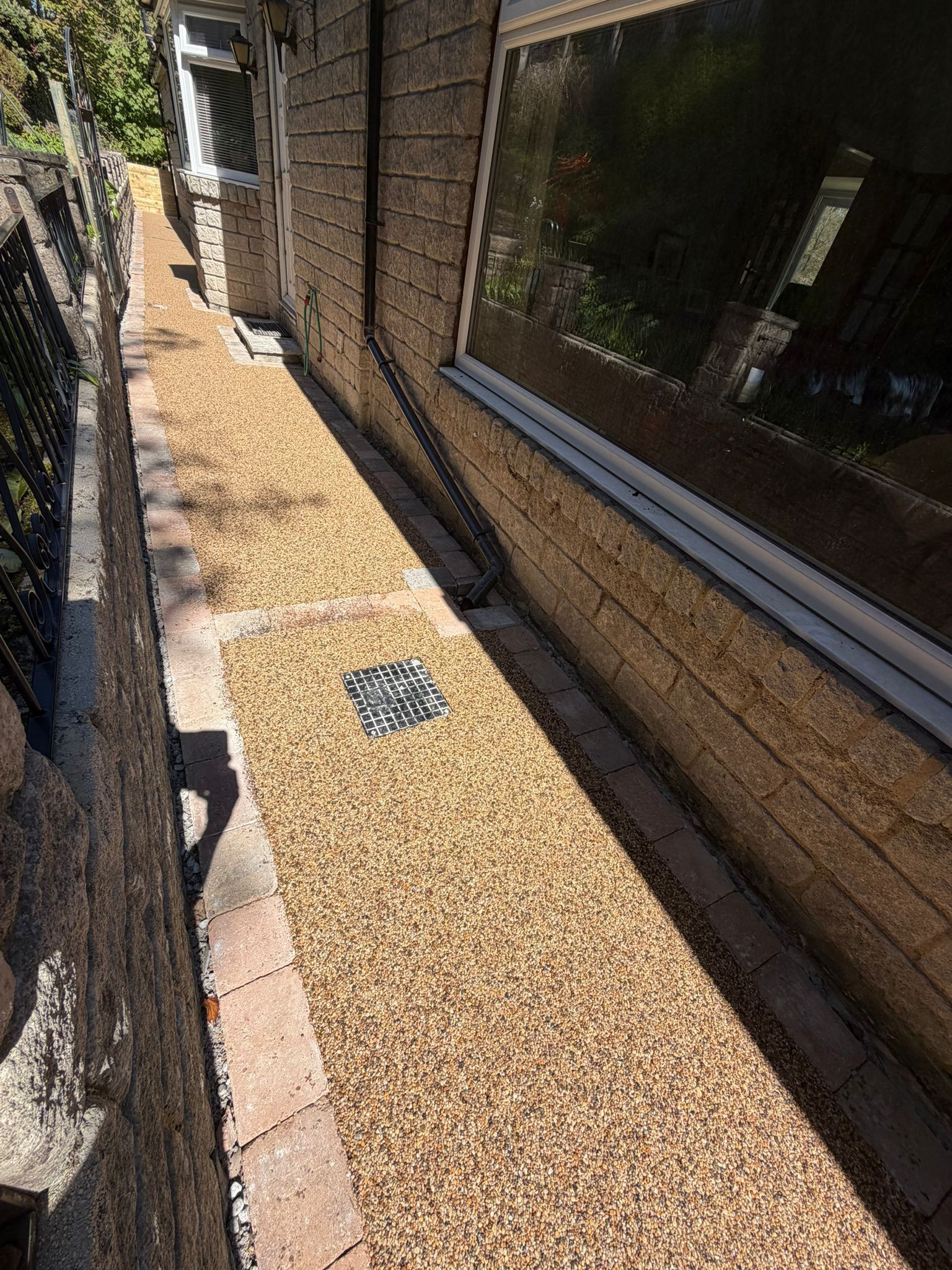 Narrow gravel walkway between a house and fence with windows along the wall.