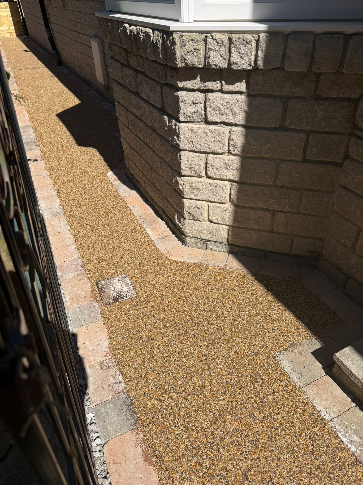 Narrow gravel walkway beside a stone retaining wall in bright sunlight