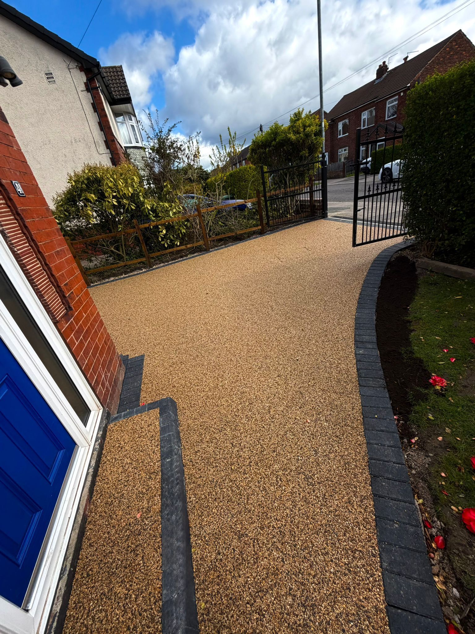 Gravel front yard path beside a house, with a gate and hedges under a cloudy sky.