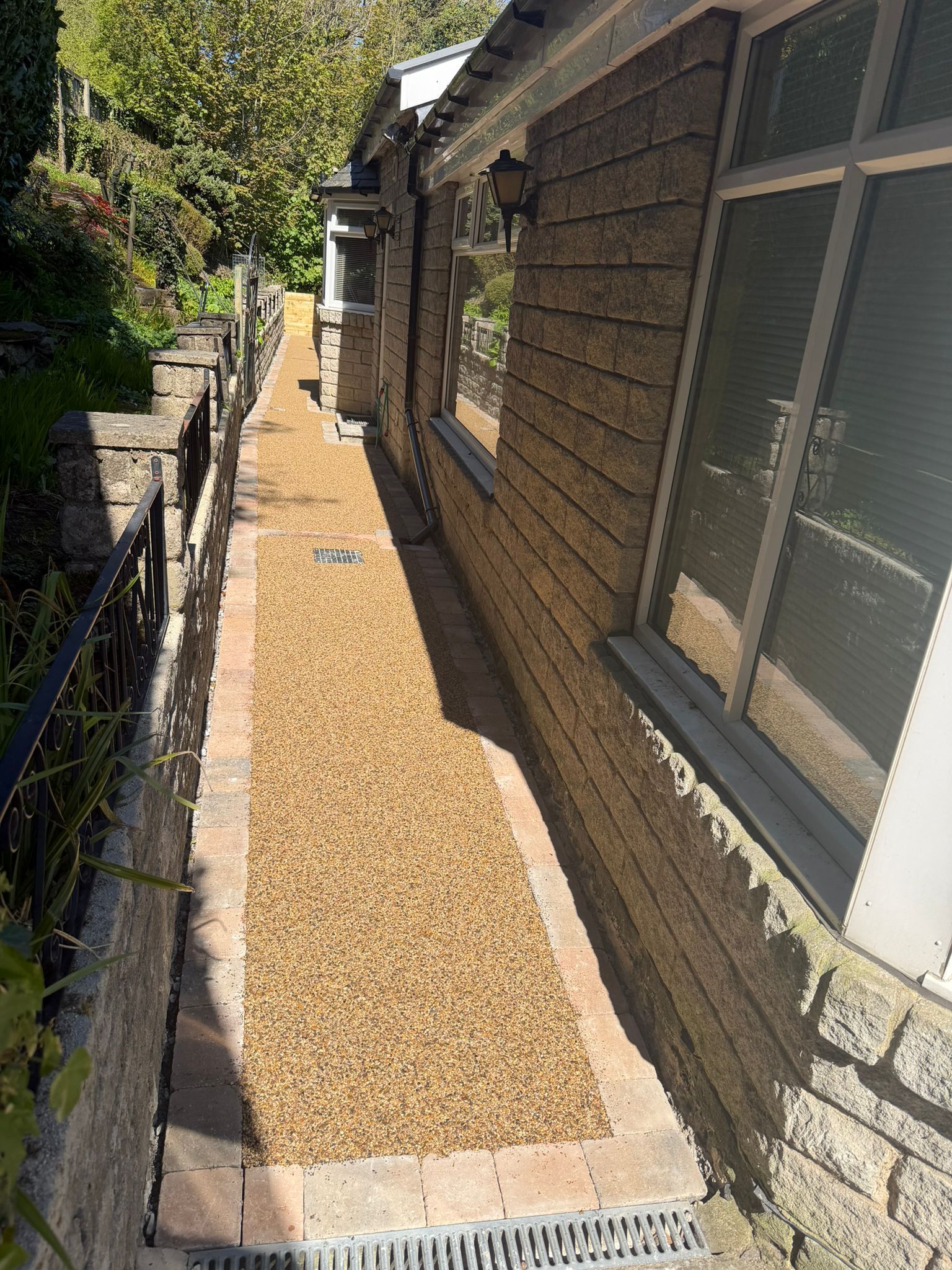 Narrow gravel side yard beside a brick house, with windows and a fence along the walkway.