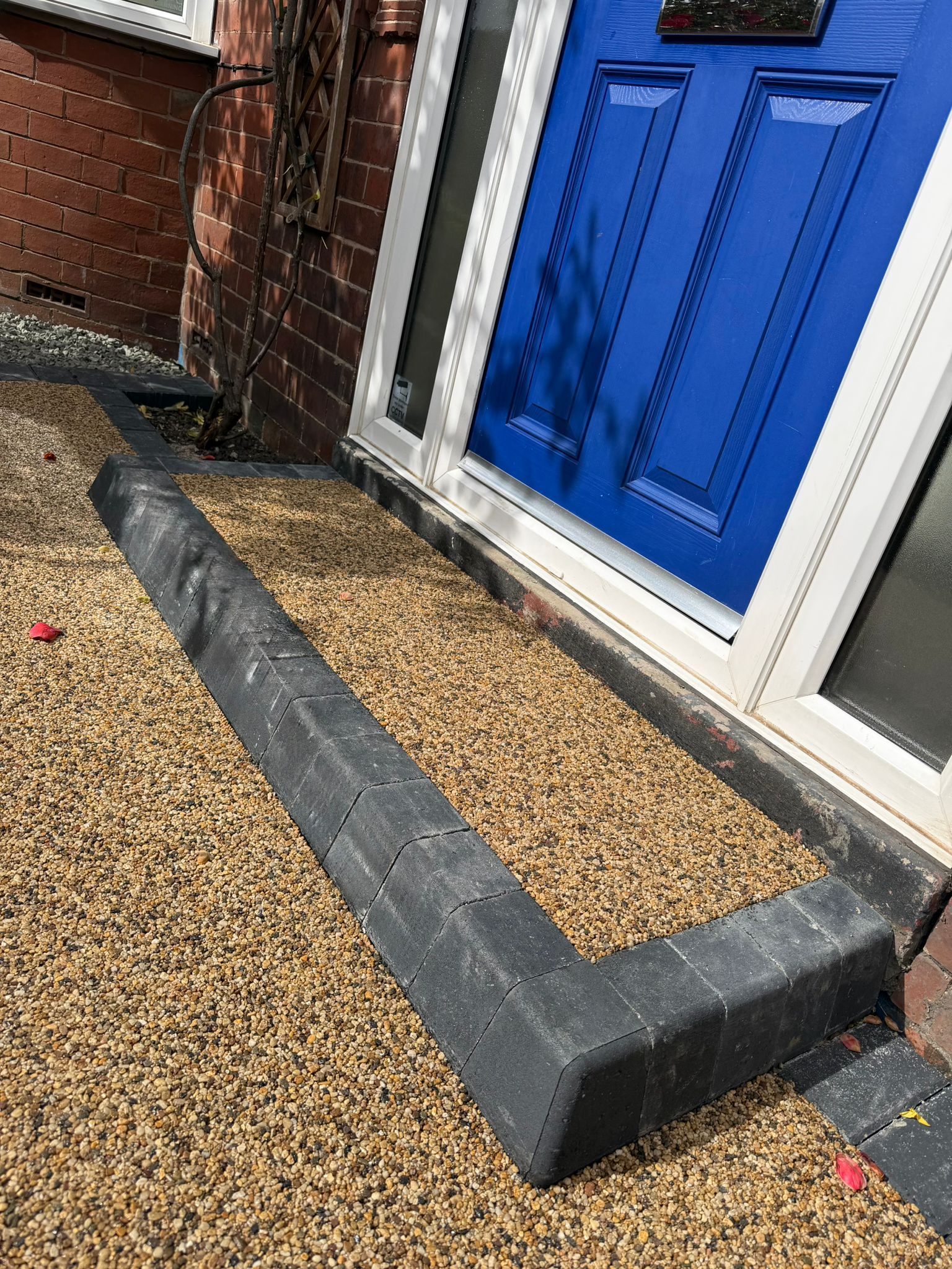 Blue front door beside a gravel path with raised black edging and brick wall to the left.