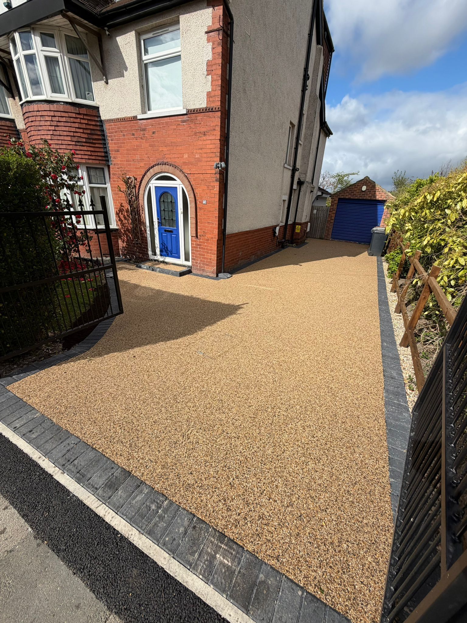 Gravel driveway beside a red-brick house with a blue front door and black fencing