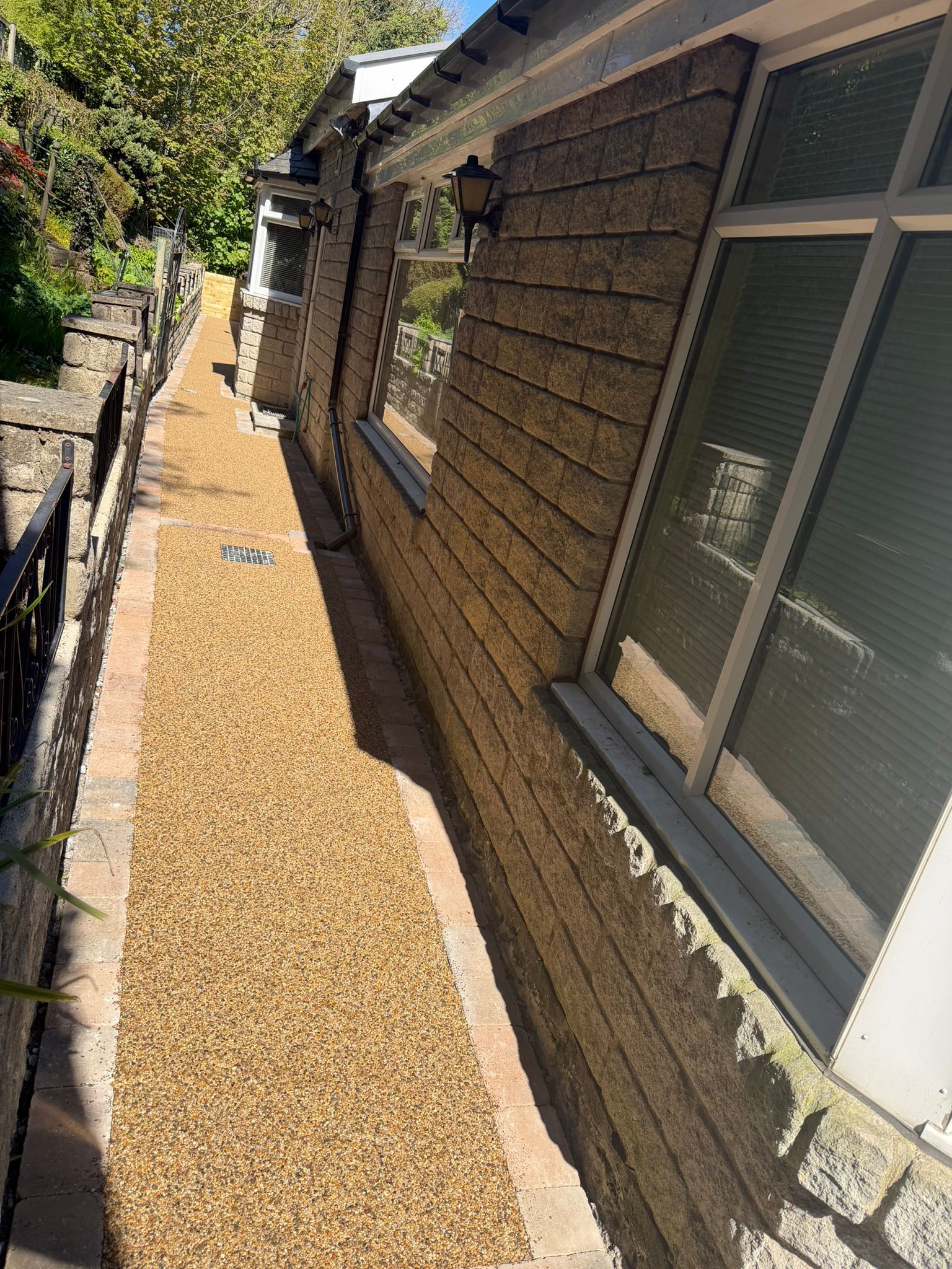 Narrow gravel side yard beside a house with windows, brick wall, and a fence along the left side.
