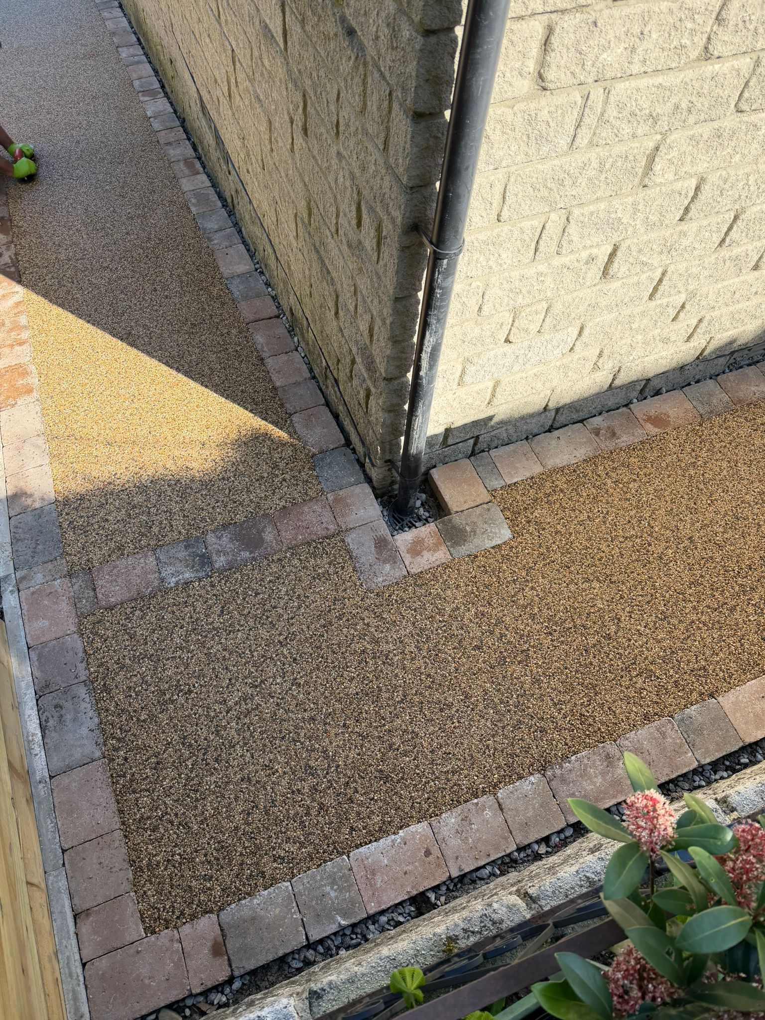 Corner of a building with gravel paving, brick edging, and a small plant at the bottom right.