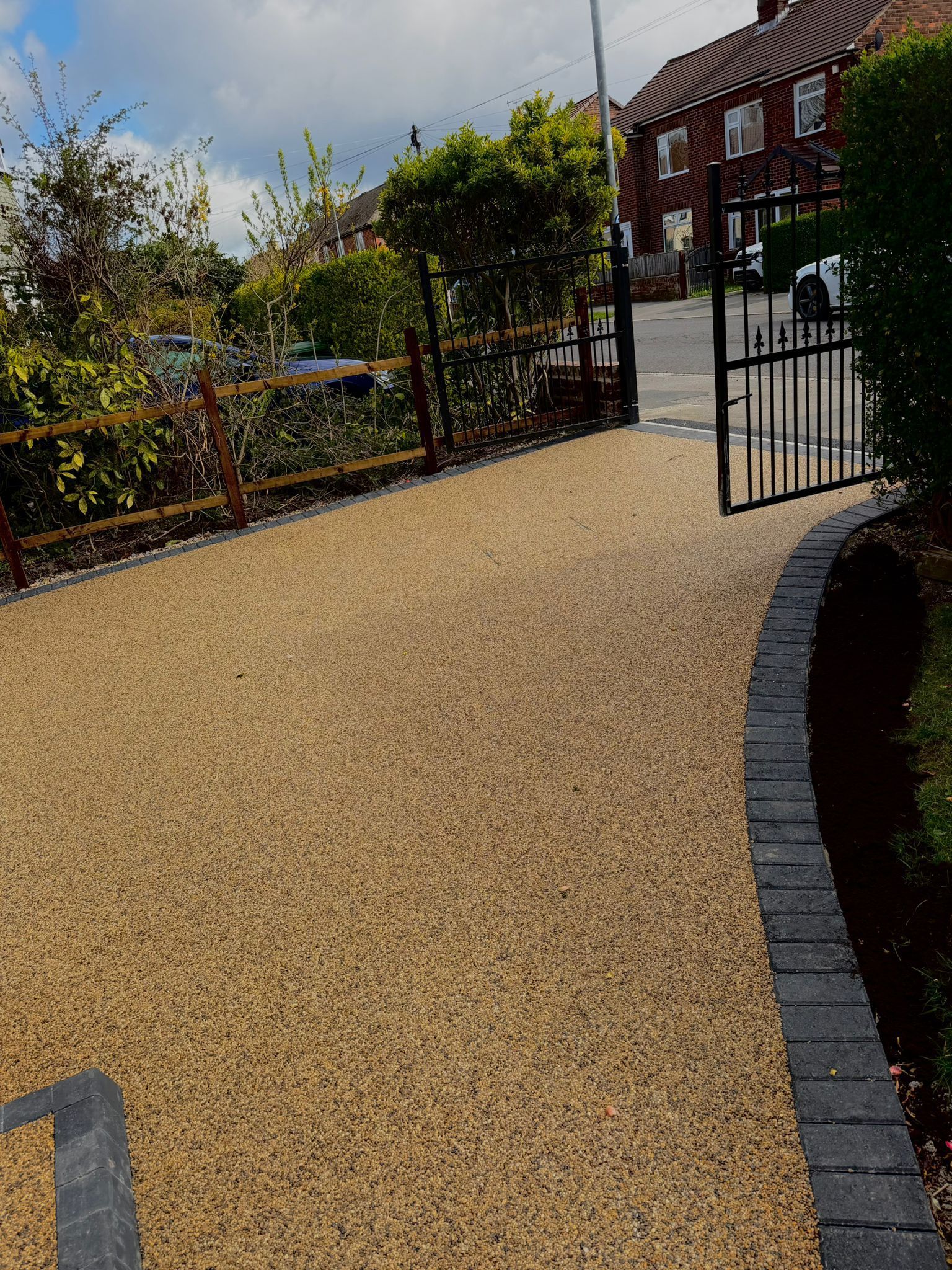 Gravel courtyard beside a black fence and brick building, with a curved stone border and gate.