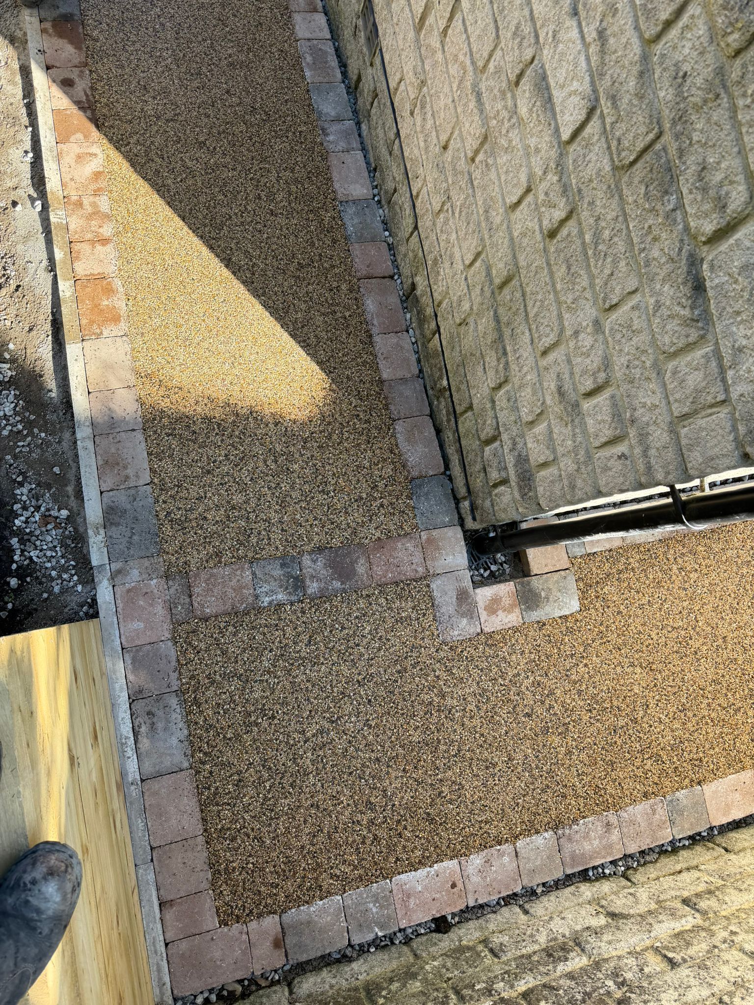 Narrow gravel walkway beside a stone wall, with a shadow and a shoe visible at the lower left.
