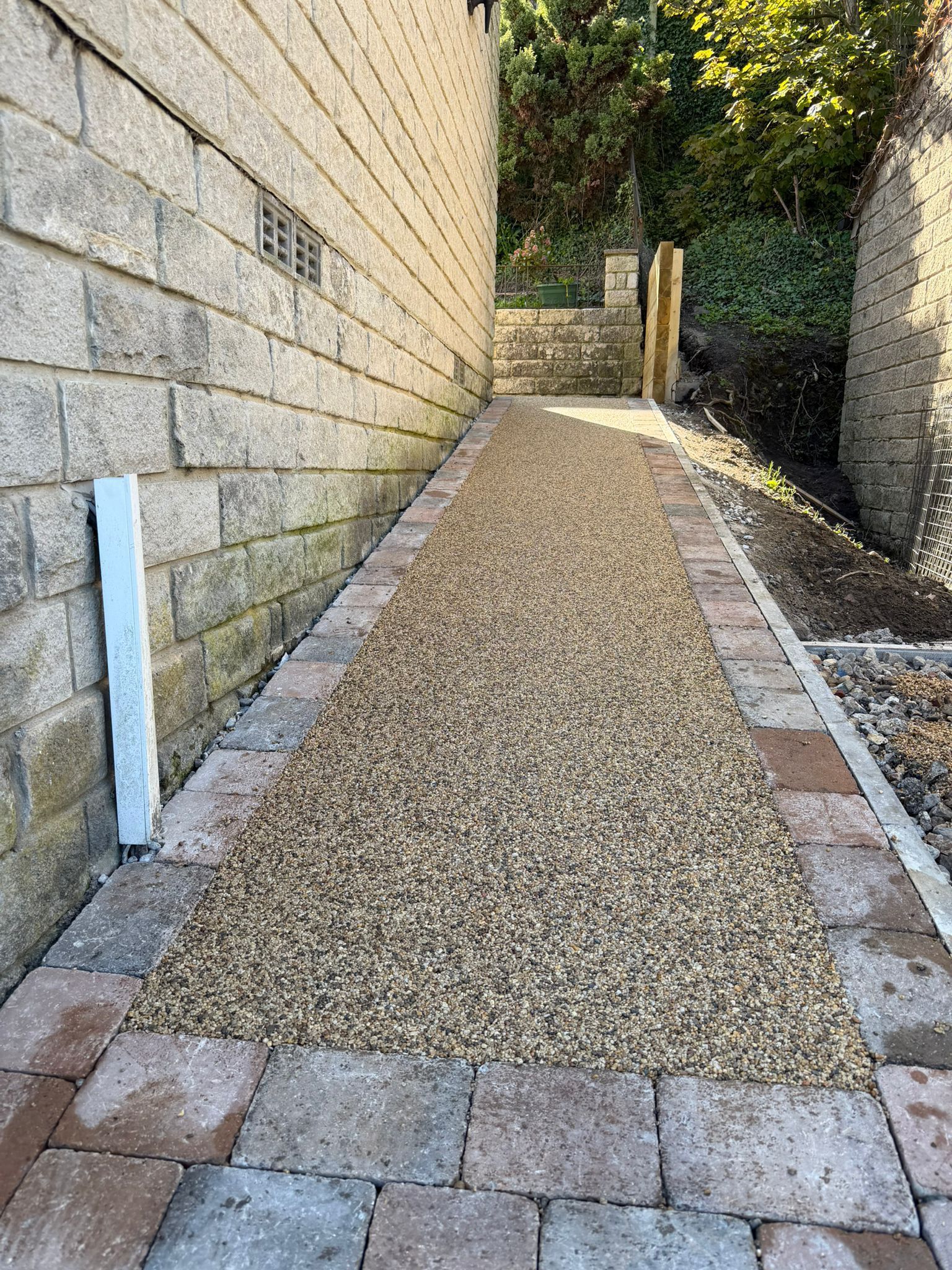 Narrow gravel path beside stone walls, leading to a gate at the end.