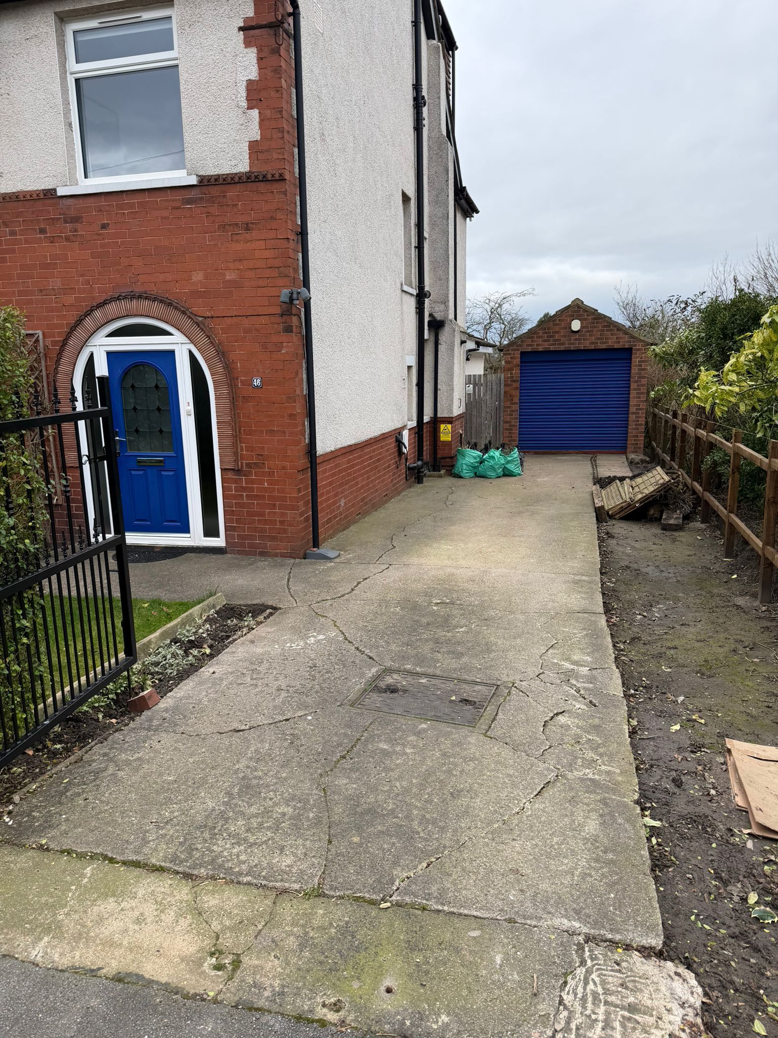 Narrow driveway beside a brick house, leading to a blue garage door and fenced side yard.
